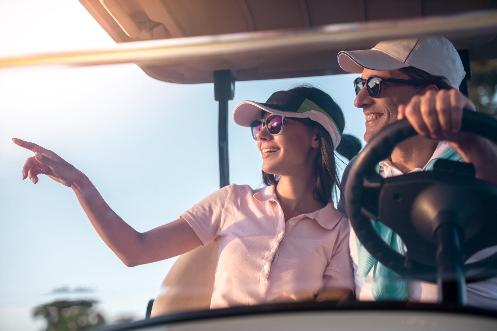 Smiling man and woman in a golf cart pointing at something